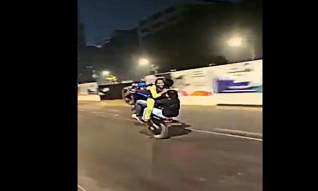 वीडियो में दिखाया गया है कि व्यक्ति बिना हेलमेट के दो महिलाओं के के साथ मोटरसाइकिल पर स्टंट कर रहा है, जिसमें एक सामने और दूसरी महिला पीछे बैठी है.